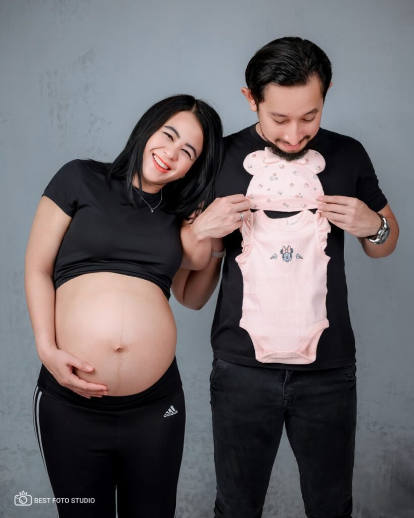 Maternity photography dengan memegang pakaian bayi dan senyum bahagia
